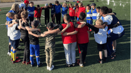 En arborist sitter högst upp i ett träd och sågar av toppen. BLå himmel i bakgrunden.