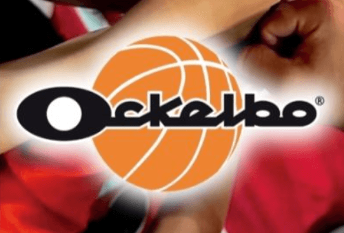 En arborist sitter högst upp i ett träd och sågar av toppen. BLå himmel i bakgrunden.